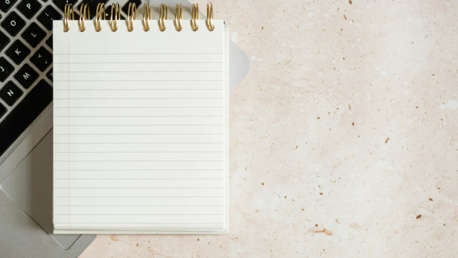 A blank notepad resting on a laptop keyboard on a plain desk, photographed from directly above