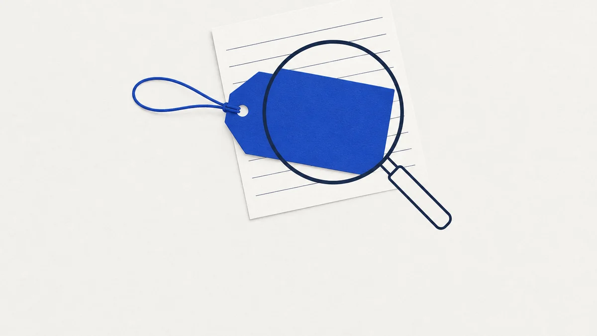 A blank cobalt price tag on a loop of string, lying on a lined sheet of paper, with a navy magnifying glass over the tag showing nothing written on it