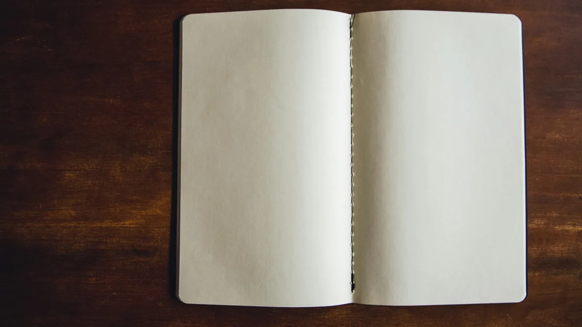 An open notebook with two blank pages, lying on a dark wooden table